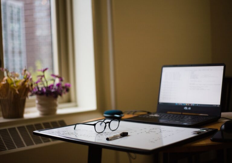 Glasses on a whiteboard next to laptop
